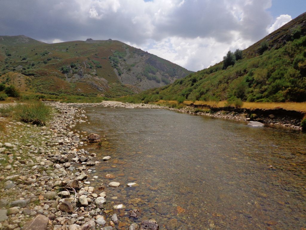 Gravas y cantos en el lecho del río entre montañas pizarrosas en la reserva natural fluvial Alto Carrión